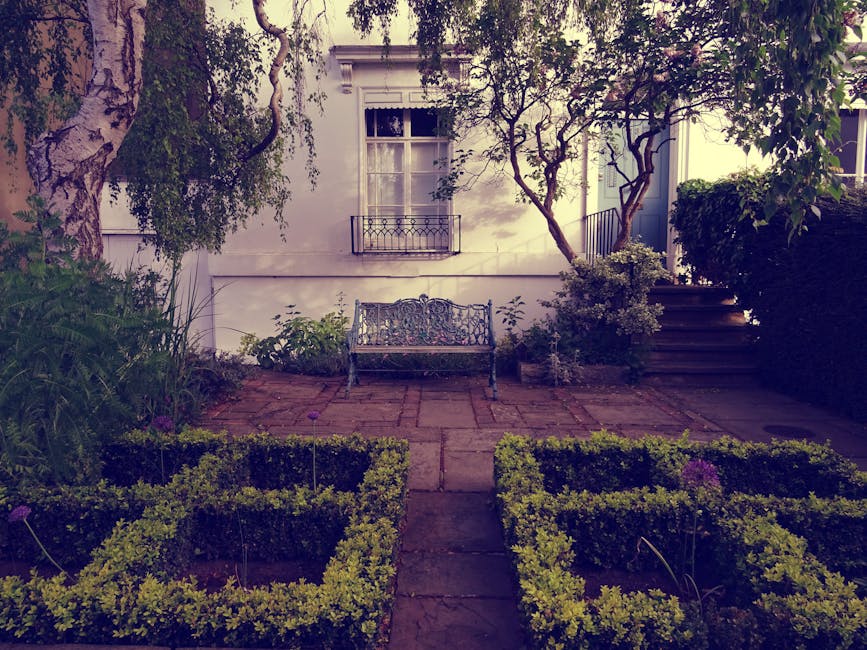 A black and white image of a narrow outdoor staircase in a residential garden setting, descending from a paved pathway made of uneven brick or stone. On the left side, a high brick wall runs parallel